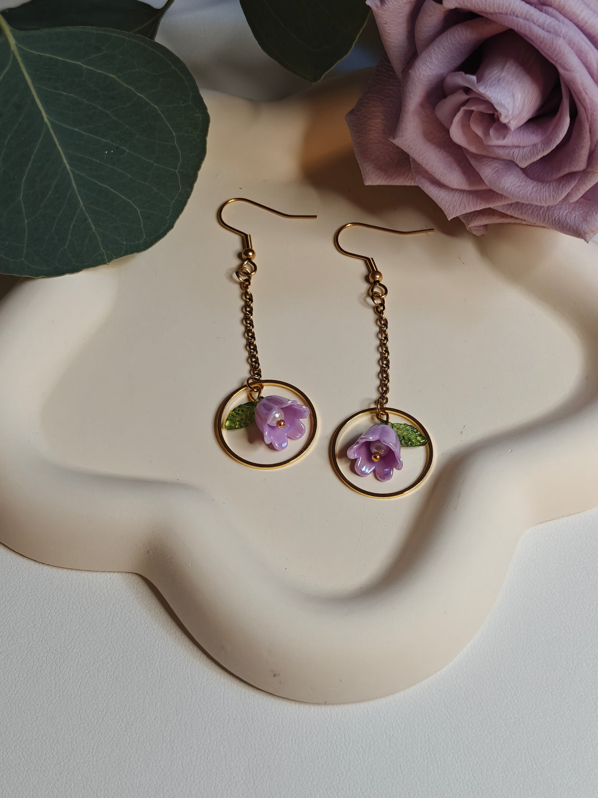 Image of the Lilac Flower Drop Earrings laying flat on a white ceramic flower shaped plate 