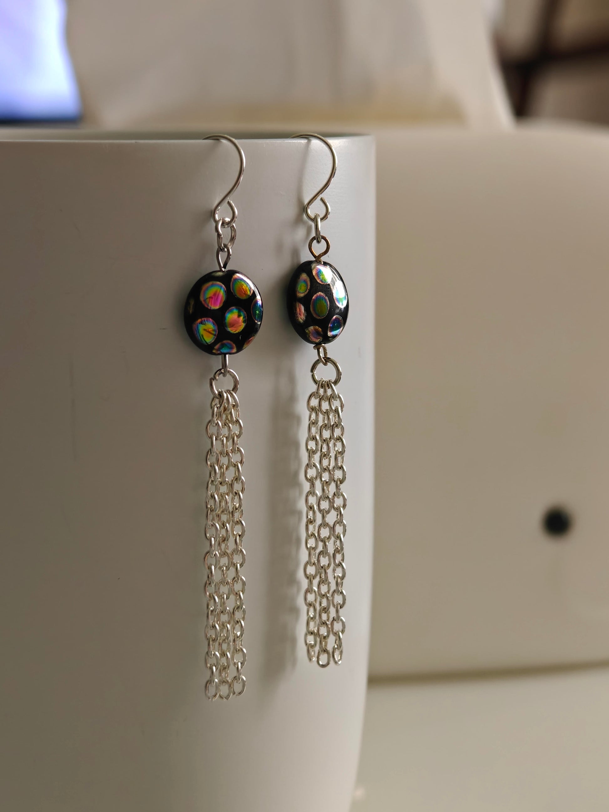 Image of the silver tone earrings featuring peacock spot flat beads attached with silver color tassels 