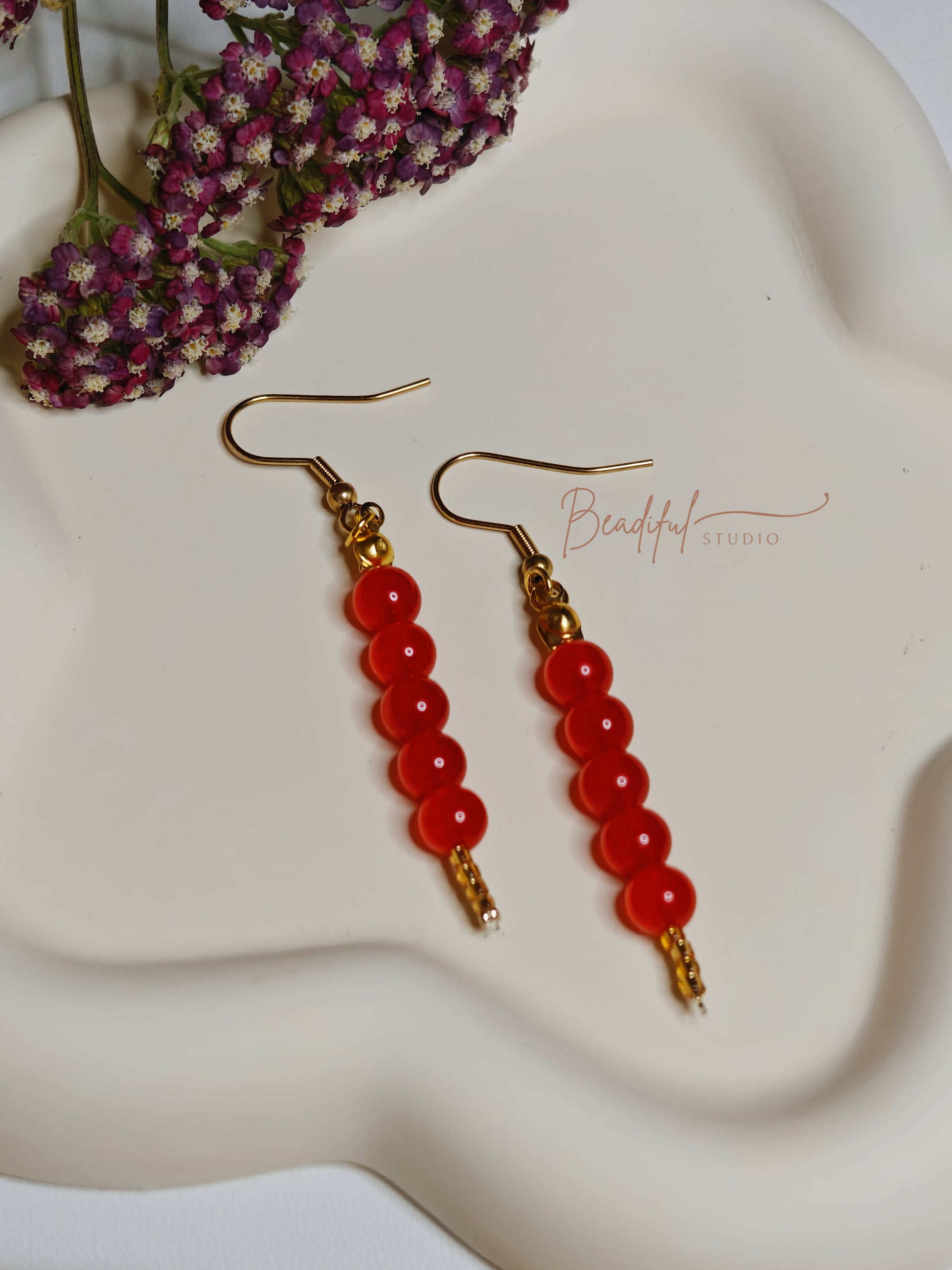 Image of the Tanghulu Earrings laying flat on a white flower shaped plate. It features five red beads and gold color earrings components 