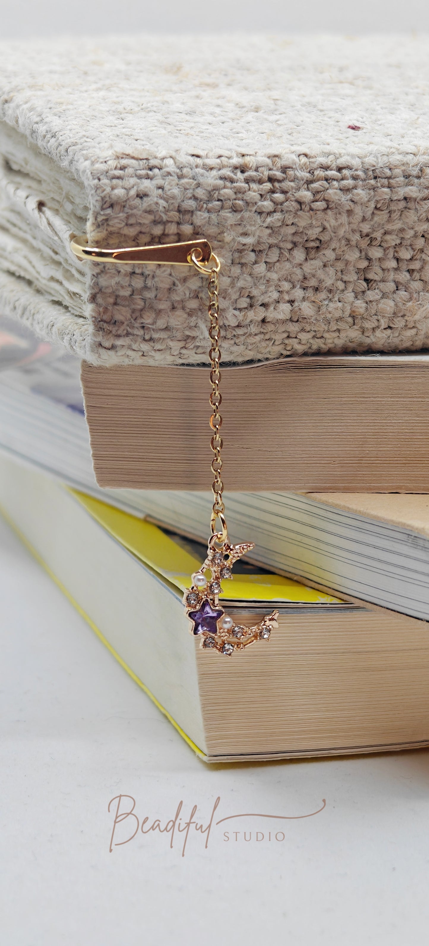 Version two of the Luna bookmark where it features a gold color hook bookmark and a medium sized half moon charm adorned with small faux white pearls and colorful gems