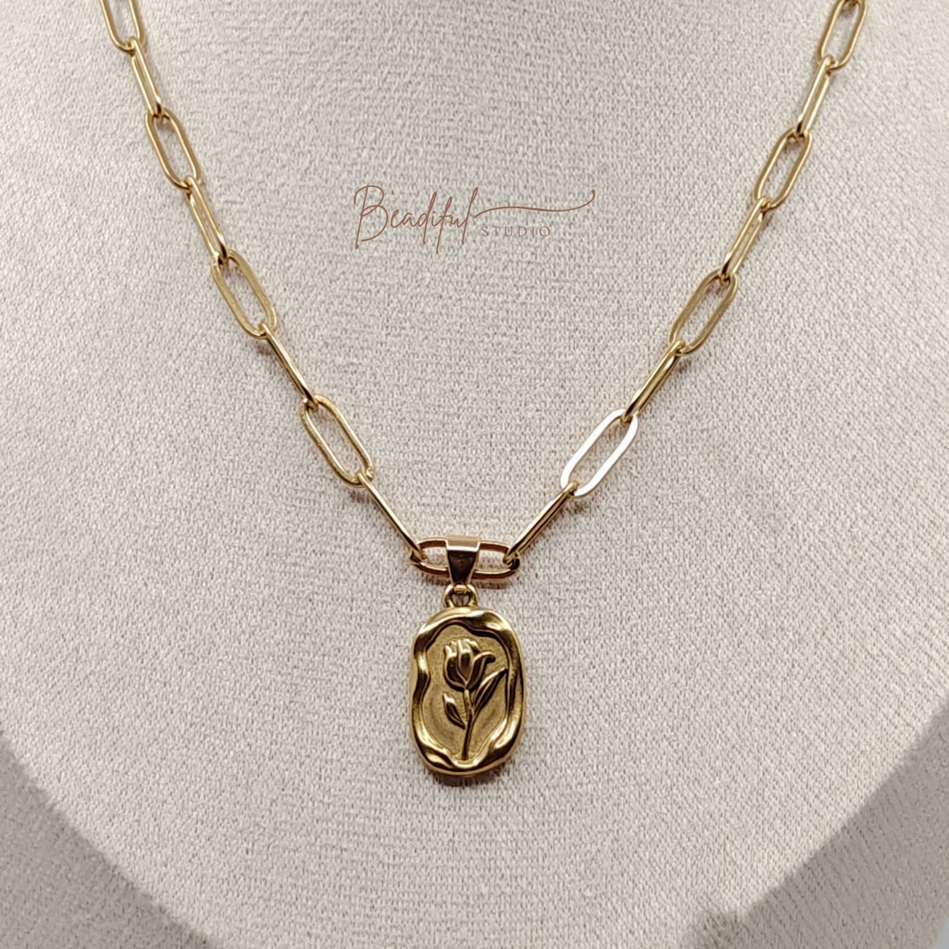 Image of a gold tone necklace that features a stainless steel gold color tulip pendant and gold color paperclip chain