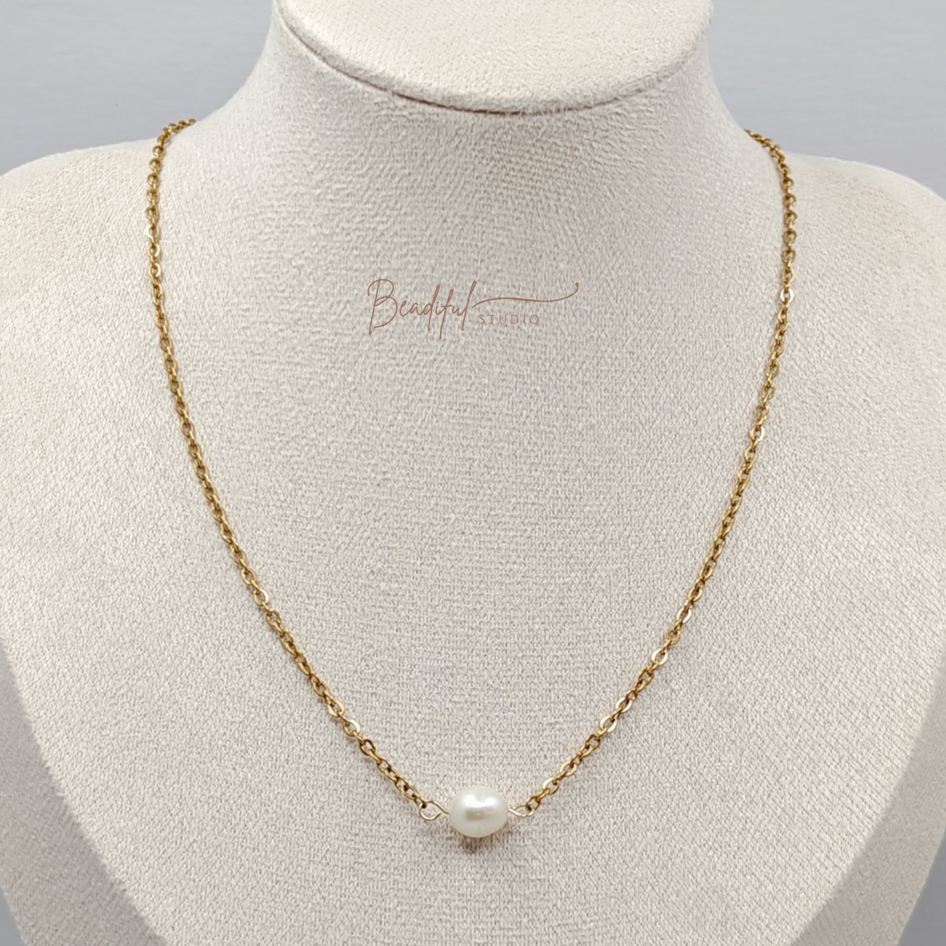 Image of the pearl necklace featuring a single white cultured freshwater pearl and gold plated stainless steel cable chain.